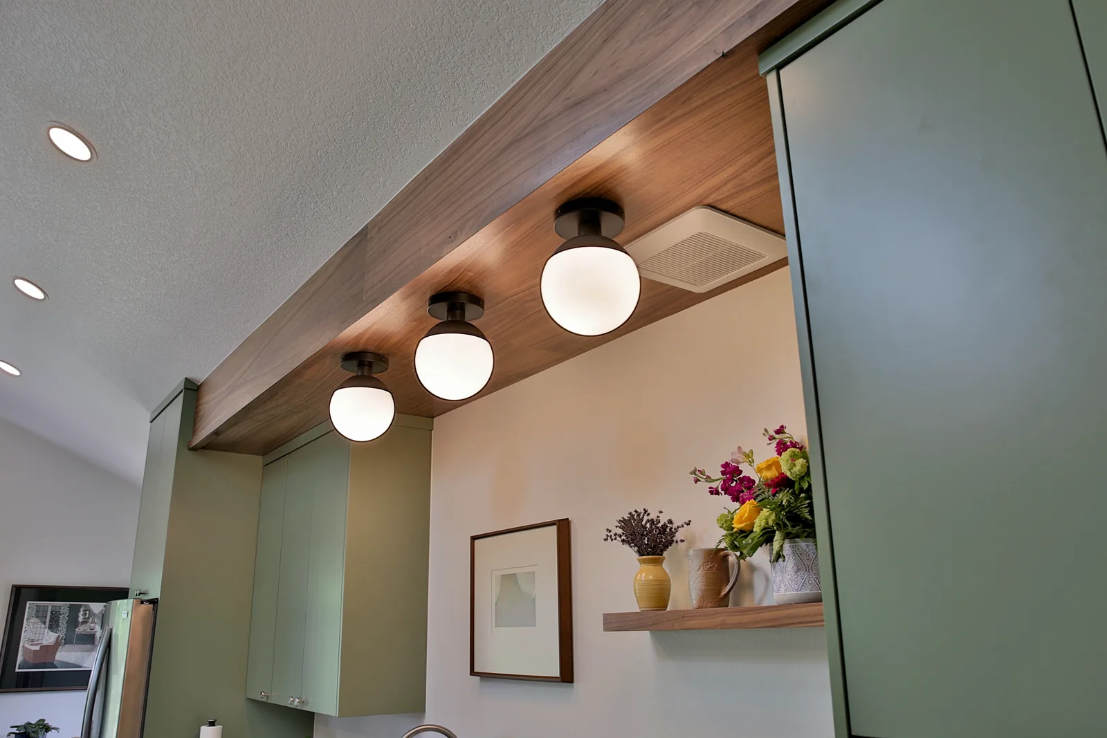 Walnut ceiling beam detail with globe fixtures over the kitchen